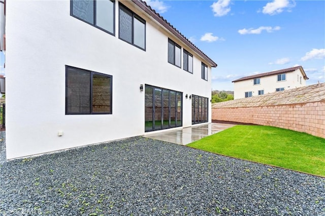 rear view of house featuring fence, stucco siding, a patio area, a tile roof, and a lawn