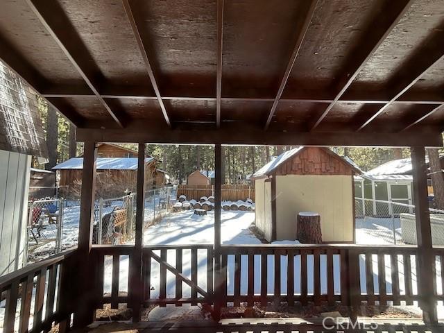 snow covered deck featuring a storage shed, an outbuilding, and fence