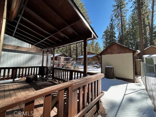 snow covered deck with an outbuilding, a patio area, and a storage unit