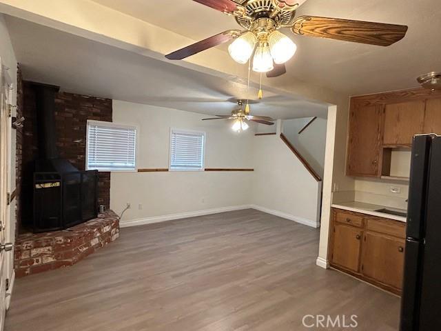 kitchen with brown cabinetry, baseboards, a wood stove, light wood-style flooring, and freestanding refrigerator