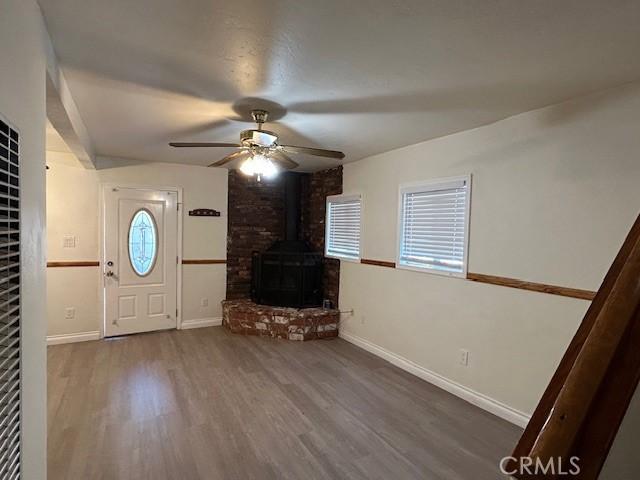 unfurnished living room featuring ceiling fan, baseboards, wood finished floors, and a wood stove