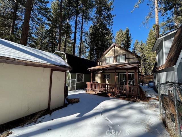 snow covered rear of property featuring stucco siding and fence