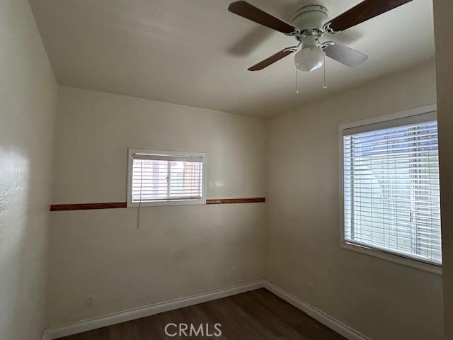 spare room featuring baseboards, dark wood-style floors, and a ceiling fan