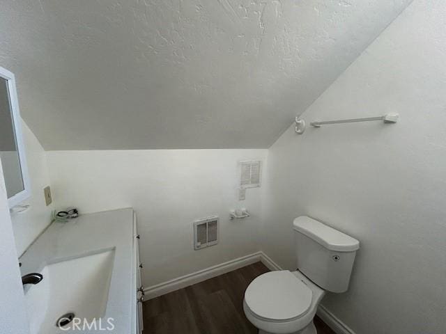 half bath with toilet, vaulted ceiling, wood finished floors, a textured ceiling, and a sink