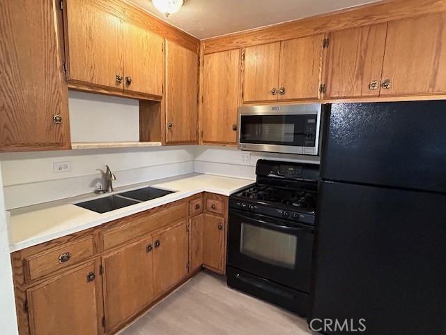 kitchen with brown cabinets, black appliances, light countertops, and a sink