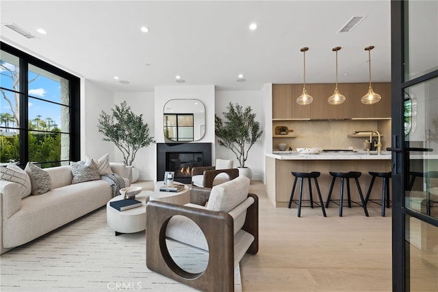 living area featuring visible vents, a glass covered fireplace, recessed lighting, light wood-style floors, and a wall of windows