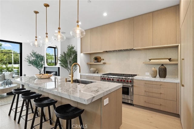 kitchen with light brown cabinetry, open shelves, a sink, backsplash, and premium stove