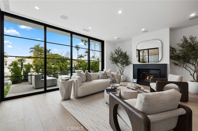 living room with visible vents, floor to ceiling windows, light wood-type flooring, recessed lighting, and a glass covered fireplace