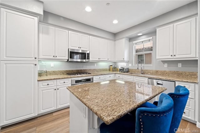 kitchen with a breakfast bar, a sink, white cabinets, appliances with stainless steel finishes, and light wood-type flooring