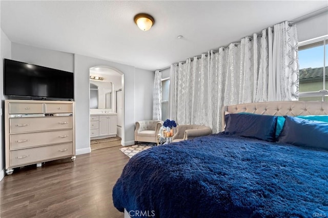 bedroom with arched walkways, connected bathroom, baseboards, and wood finished floors