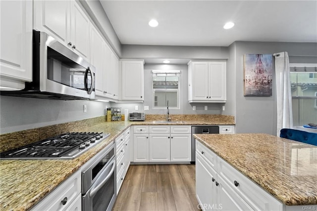 kitchen featuring light stone counters, appliances with stainless steel finishes, wood finished floors, white cabinetry, and a sink