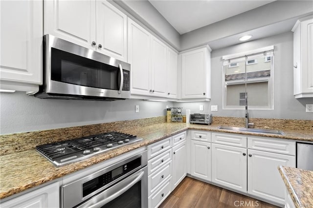 kitchen with a sink, appliances with stainless steel finishes, dark wood-style flooring, and white cabinetry