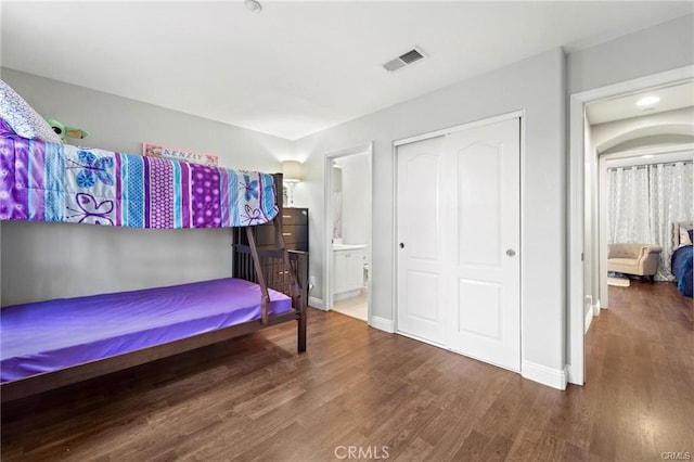 bedroom with visible vents, baseboards, wood finished floors, a closet, and ensuite bath