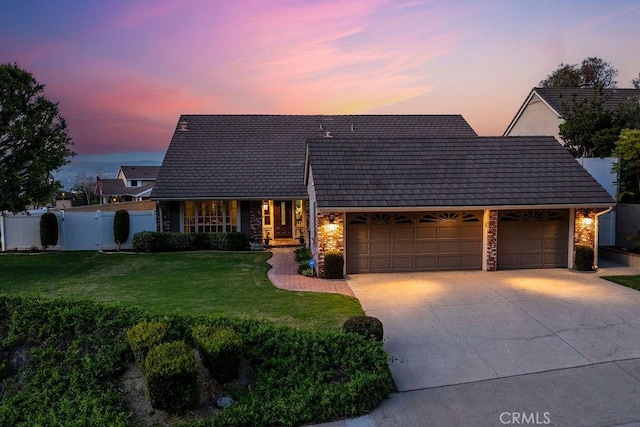 view of front of property featuring a front yard, fence, driveway, stone siding, and a garage