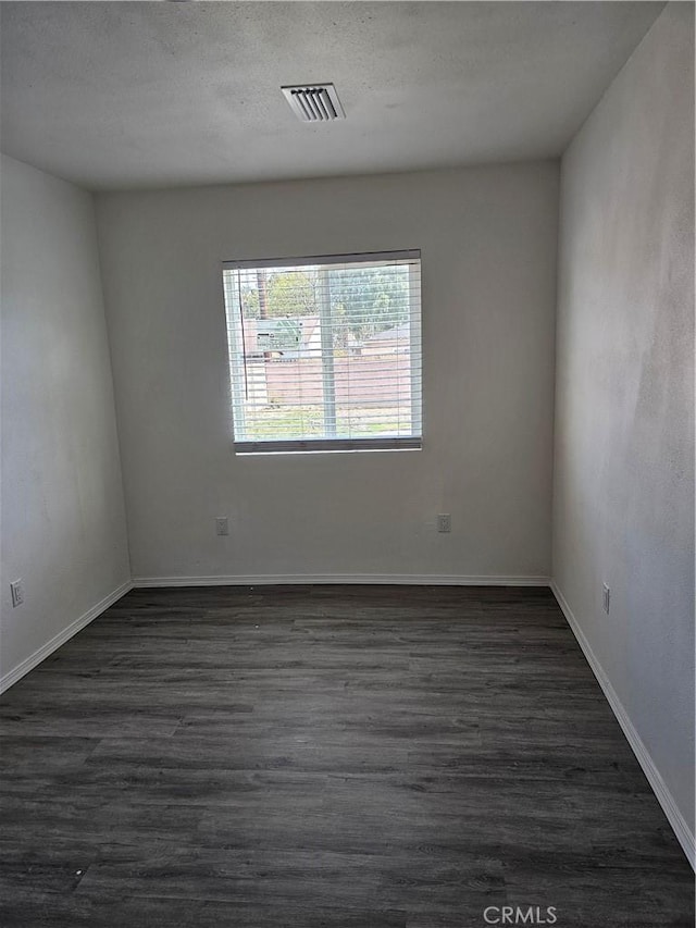 empty room featuring dark wood-type flooring, baseboards, visible vents, and a textured ceiling