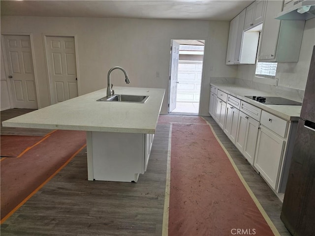 kitchen featuring a sink, black electric stovetop, under cabinet range hood, an island with sink, and dark wood-style flooring