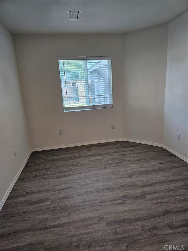 unfurnished room featuring dark wood-style floors, visible vents, and baseboards