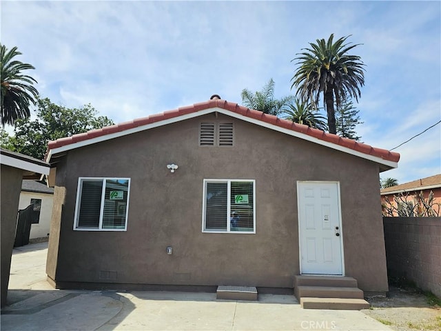 back of house featuring fence, stucco siding, entry steps, crawl space, and a tile roof