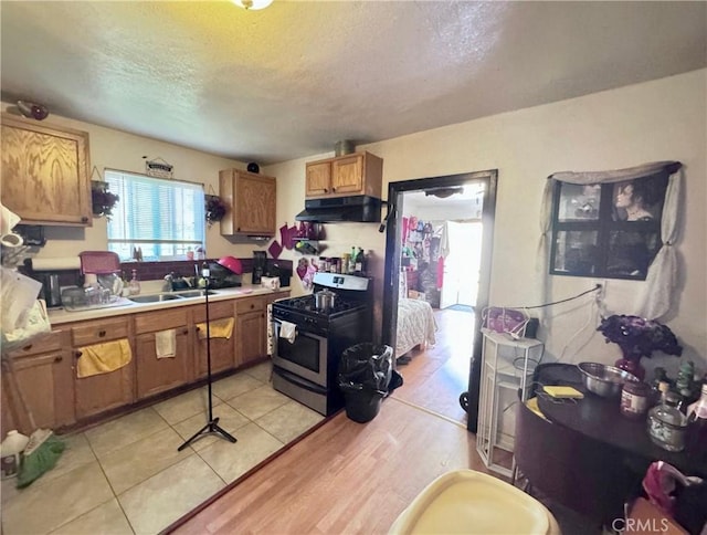 kitchen with under cabinet range hood, brown cabinets, stainless steel gas stove, a textured ceiling, and a sink