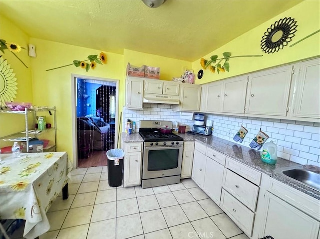 kitchen featuring stainless steel gas stove, light tile patterned floors, under cabinet range hood, and decorative backsplash