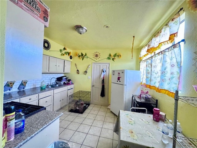 kitchen with decorative backsplash, freestanding refrigerator, light tile patterned flooring, white cabinetry, and a sink