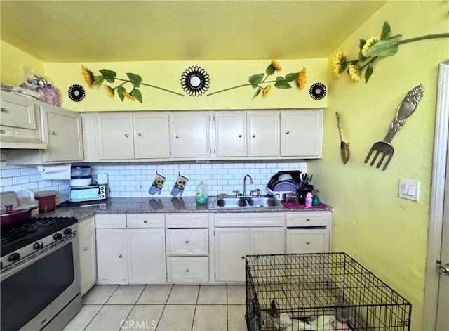 kitchen featuring light tile patterned floors, gas stove, a sink, under cabinet range hood, and tasteful backsplash