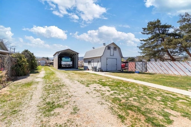 view of barn featuring a carport, a lawn, fence, and driveway