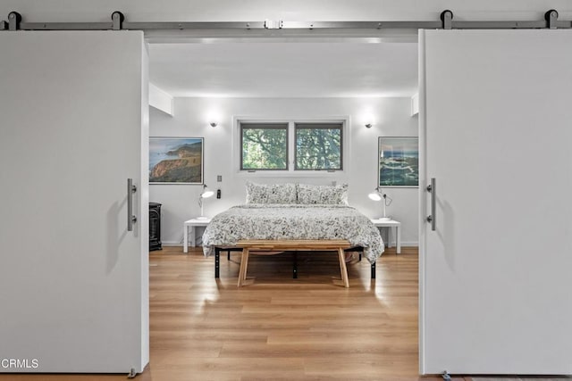 bedroom featuring a barn door, light wood-style flooring, and freestanding refrigerator