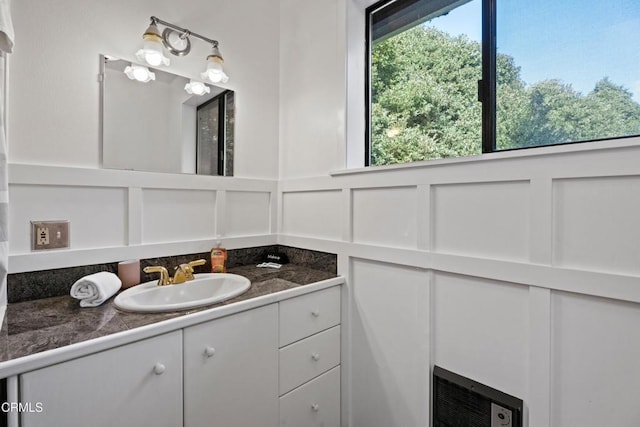 bathroom featuring heating unit, a healthy amount of sunlight, vanity, and a decorative wall