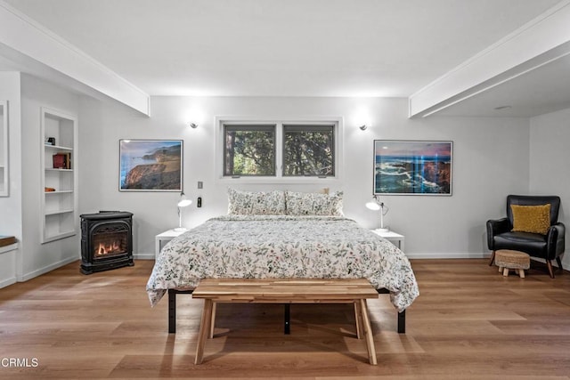 bedroom featuring baseboards, light wood-style flooring, and a wood stove