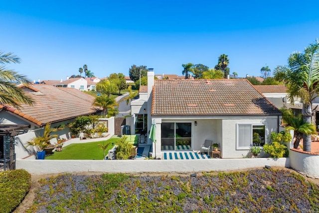 rear view of house featuring a tiled roof, stucco siding, a chimney, a fenced backyard, and a patio area