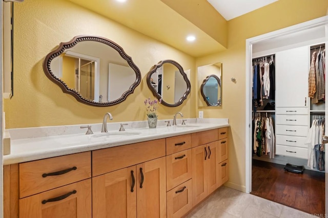 bathroom with double vanity, a walk in closet, and a sink