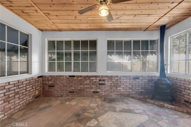 unfurnished sunroom featuring wooden ceiling, a wood stove, and ceiling fan