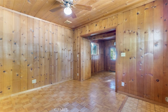 unfurnished room with visible vents, ceiling fan, baseboards, wood walls, and wood ceiling