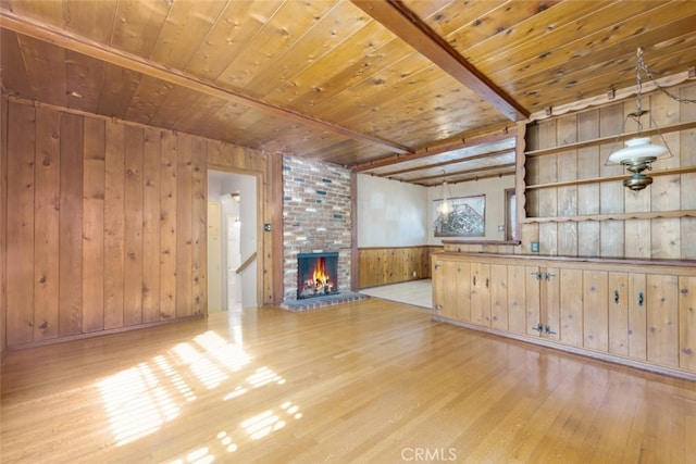 unfurnished living room with wooden walls, beam ceiling, wooden ceiling, a fireplace, and wood finished floors