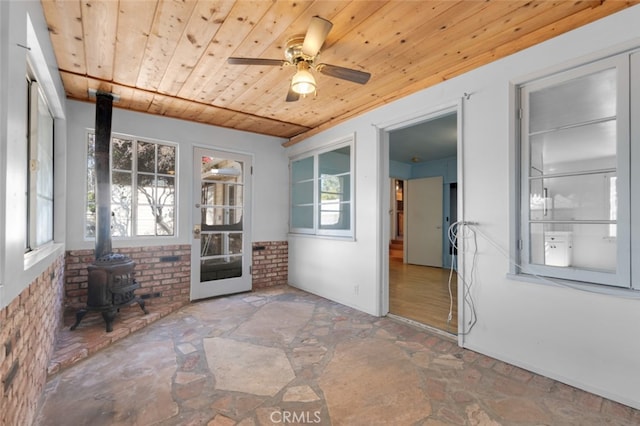 unfurnished sunroom with ceiling fan, plenty of natural light, wooden ceiling, and a wood stove