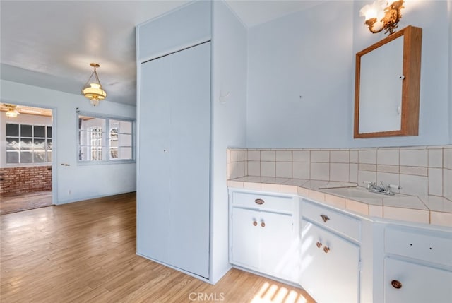 interior space with light wood finished floors, tile counters, decorative light fixtures, white cabinetry, and a sink