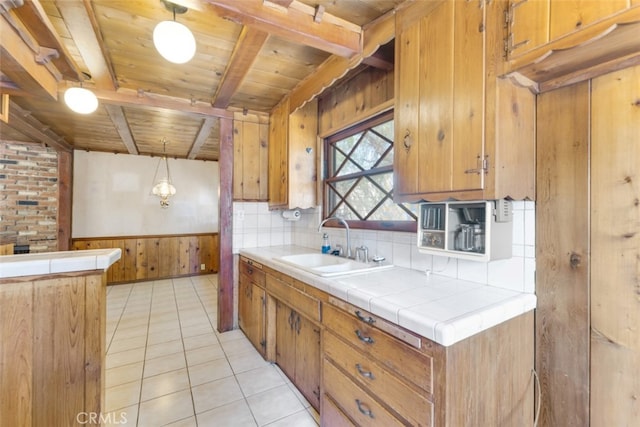 kitchen featuring beam ceiling, a sink, wooden ceiling, wainscoting, and light tile patterned floors