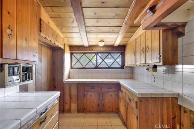 kitchen featuring brown cabinetry, beamed ceiling, tile countertops, and backsplash