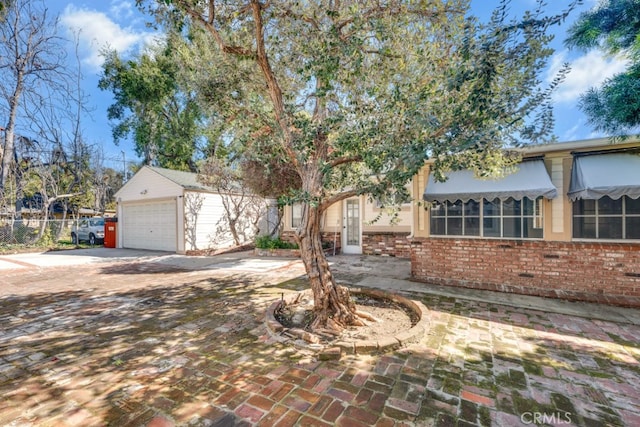 view of front of home featuring brick siding, an outdoor structure, driveway, and fence