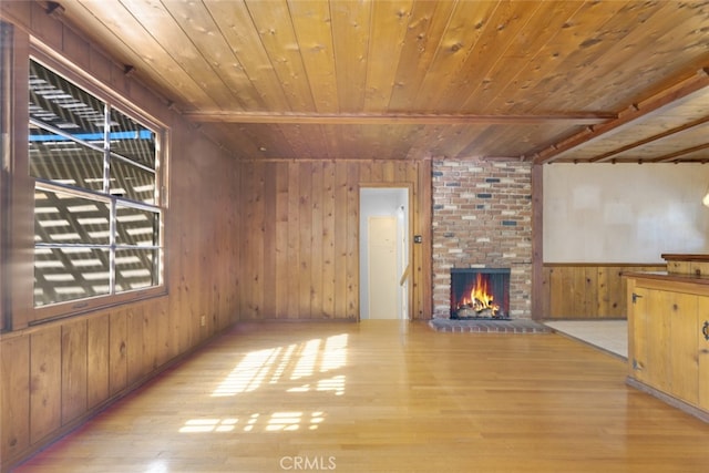 unfurnished living room with beamed ceiling, wood finished floors, wooden walls, a fireplace, and wood ceiling