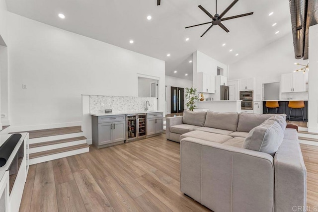 living room with beverage cooler, high vaulted ceiling, recessed lighting, ceiling fan, and light wood-type flooring