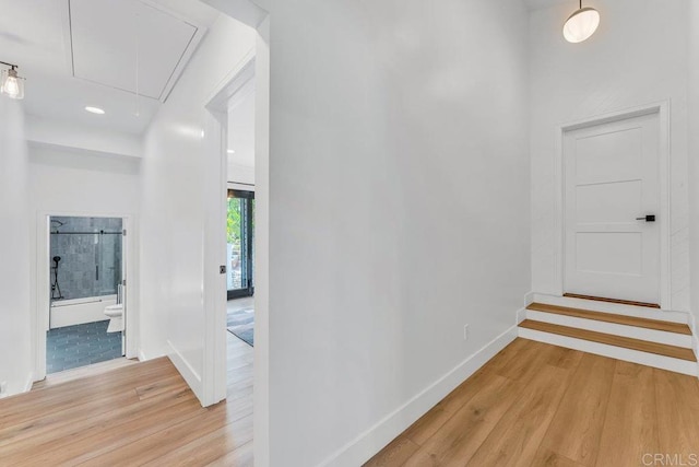 corridor featuring baseboards, light wood-style floors, and attic access