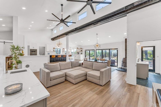 living area with recessed lighting, high vaulted ceiling, ceiling fan, and light wood finished floors