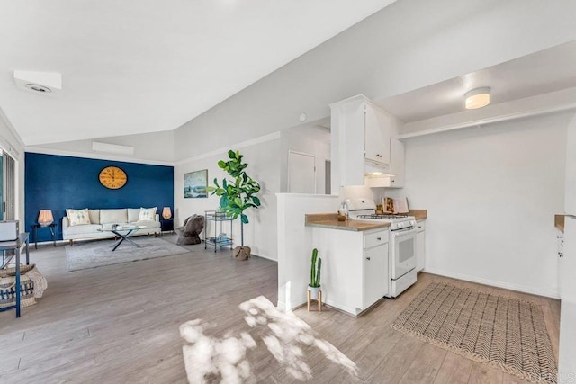 kitchen featuring light wood finished floors, lofted ceiling, gas range gas stove, under cabinet range hood, and white cabinetry