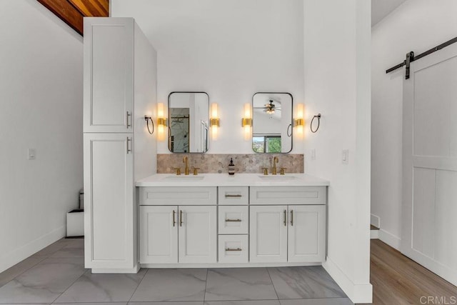 full bath featuring a sink, baseboards, backsplash, and double vanity