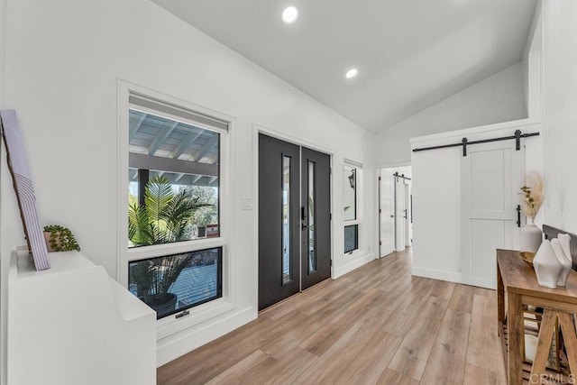 entrance foyer featuring recessed lighting, a barn door, light wood-style floors, and vaulted ceiling