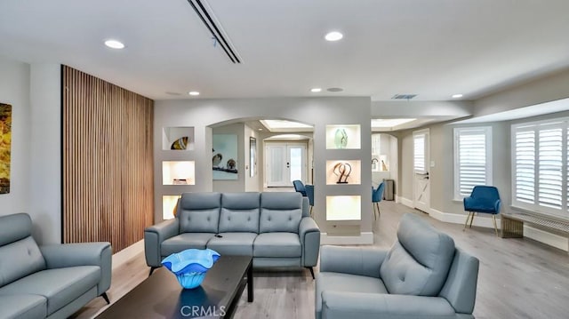 living area featuring visible vents, baseboards, recessed lighting, light wood-style flooring, and arched walkways