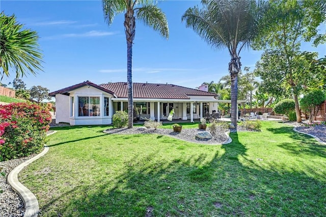 rear view of house featuring stucco siding, a lawn, a tile roof, and fence