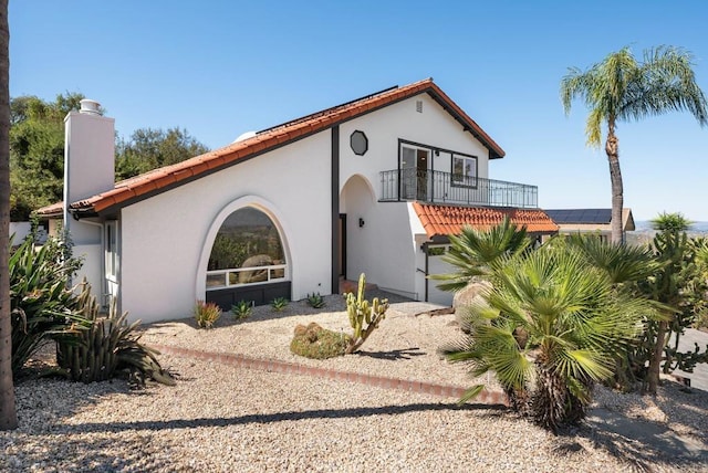 mediterranean / spanish-style home featuring stucco siding, a chimney, and a balcony